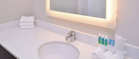 Un bagno d'albergo con un lavandino bianco, uno specchio e articoli da toilette.
