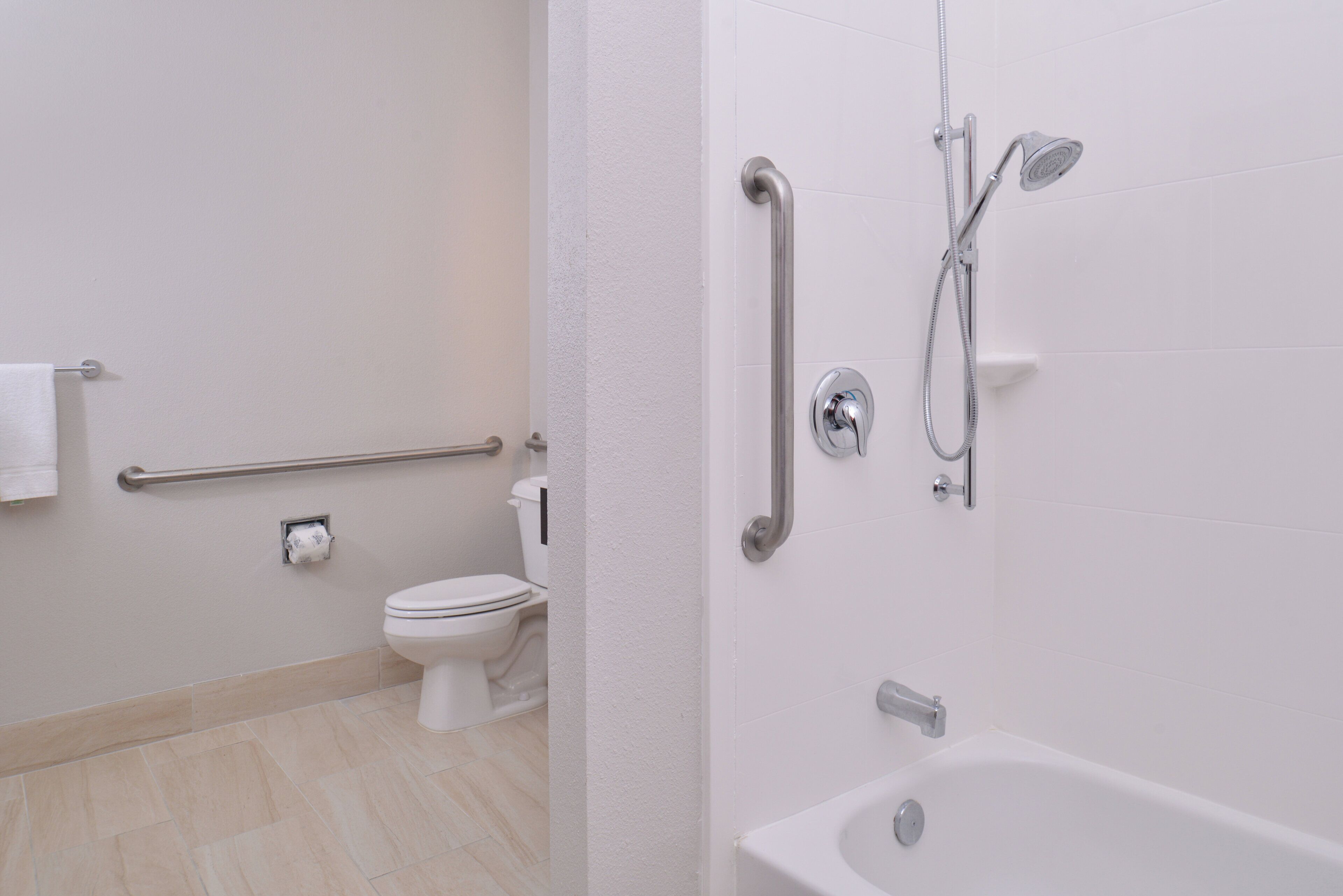 Et badeværelse med toilet, gelænder, bruser med håndbruser og badekar.