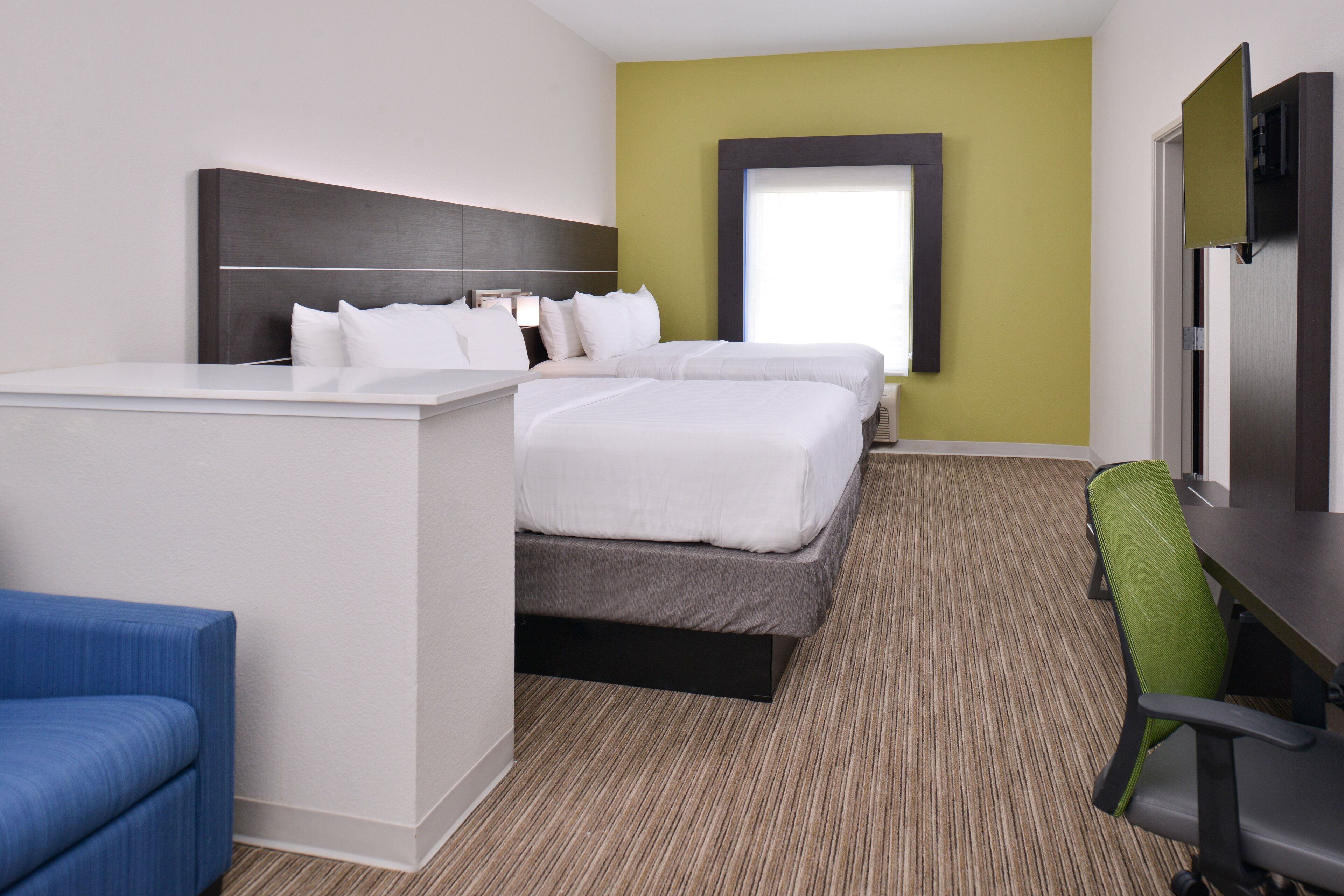 A hotel room with a bed, a desk, a chair, and a television.