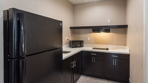 Una cocina compacta con muebles oscuros, un refrigerador negro, un microondas y un lavamanos.