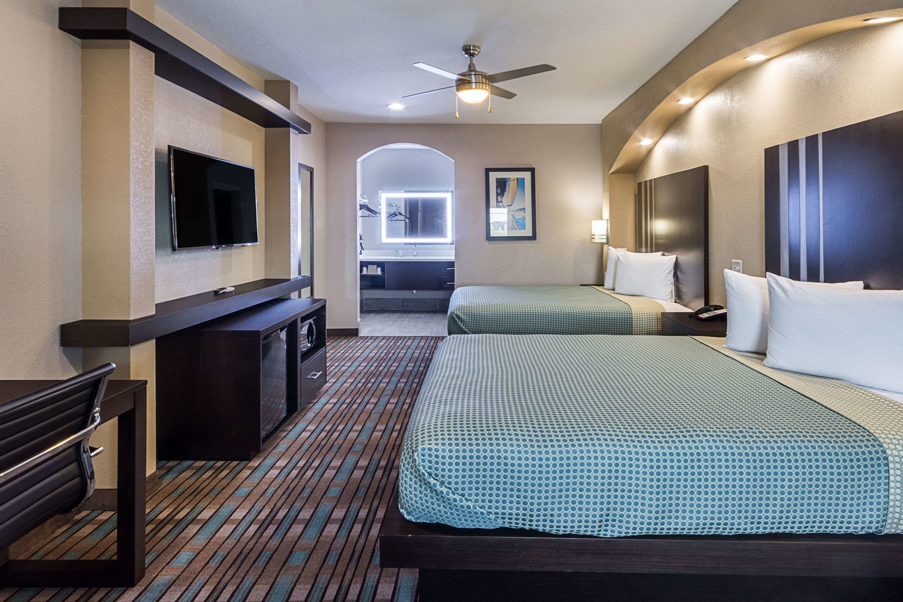 A hotel room with two beds, a TV, a desk, and a ceiling fan.