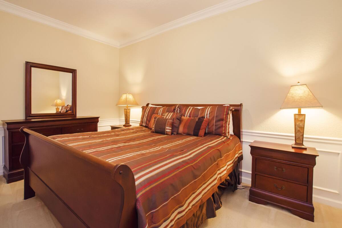 A bedroom with a large bed, two bedside tables, a nightstand, and a mirror on the wall.