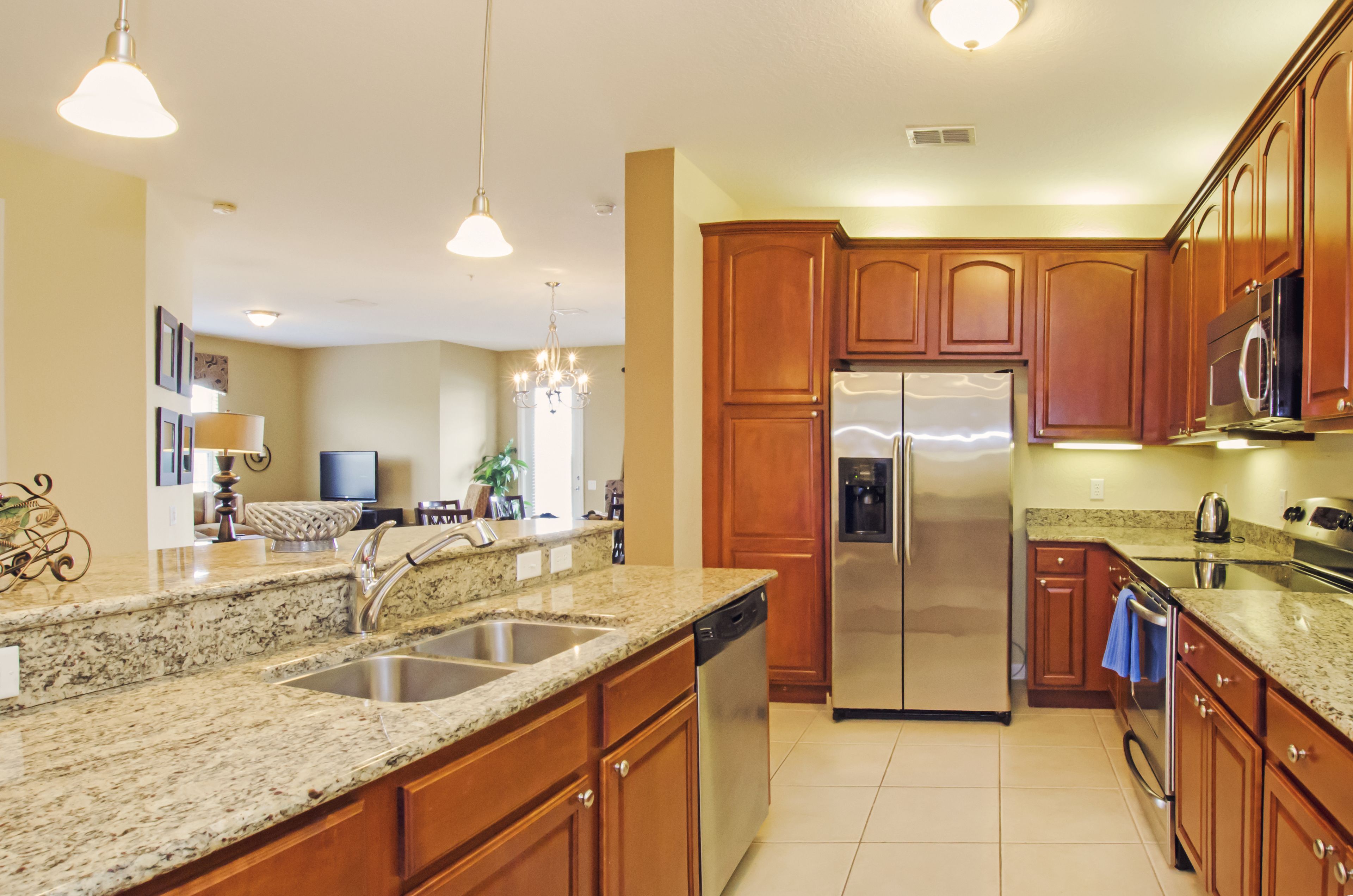 A modern kitchen with granite countertops, stainless steel appliances, wooden cabinets, and pendant lighting.