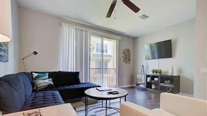 A modern living room with a sectional sofa, a round coffee table, a white armchair, and a TV mounted on the wall.