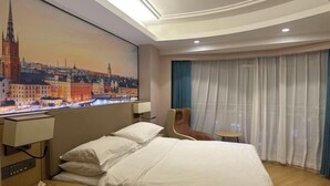 A hotel room with a bed, a nightstand, a chair, a table, a painting of a cityscape, and a window with curtains. - Vienna International Hotel (Changzhou Hutang) (Changzhou)