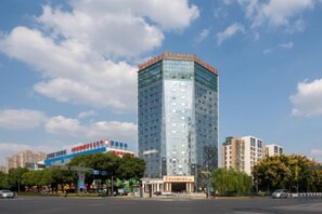 A multi-story building with a glass facade, located in an urban setting with other buildings in the background. - Vienna International Hotel (Changzhou Hutang) (Changzhou)