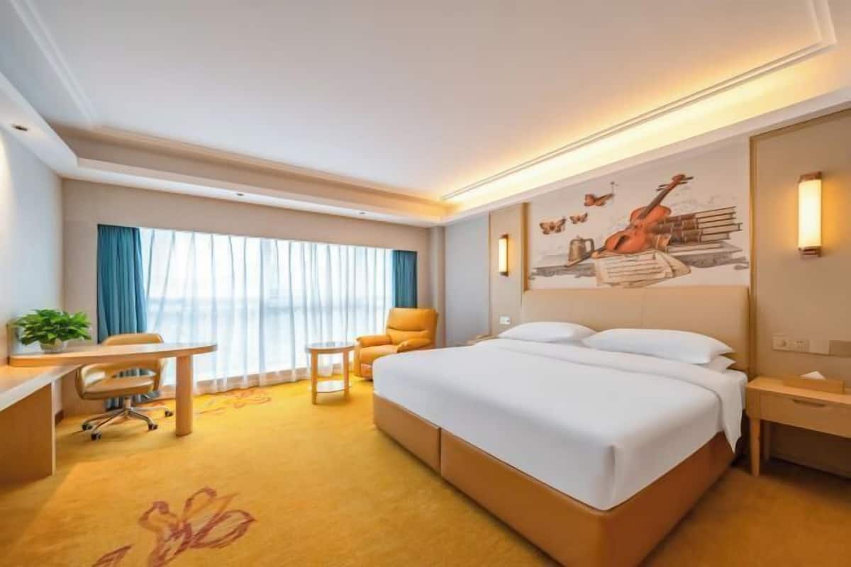 A hotel room with a large bed, a desk, a chair, a small table, and a wall with a mural.