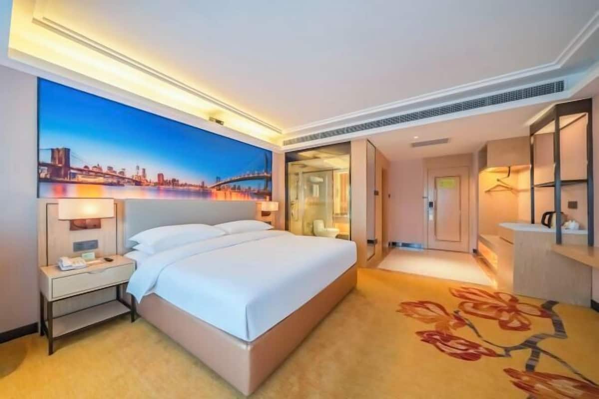 A hotel room with a bed, nightstand, lamp, and a painting of a cityscape.