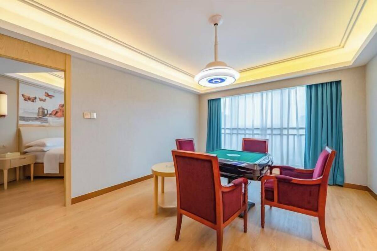 A hotel room with a dining table, chairs, a pool table, and a large window with curtains.