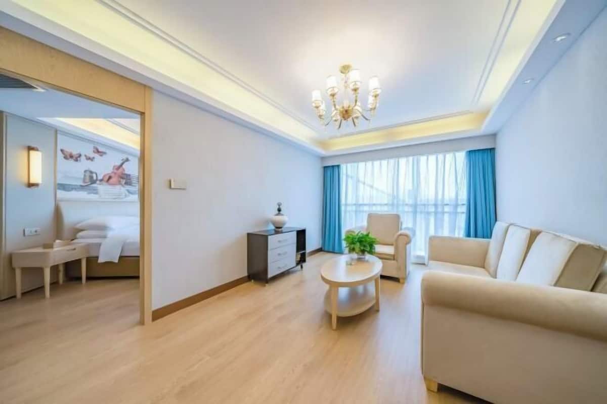 A modern living room with a sofa, a small table, a chair, a bed, and a painting on the wall.