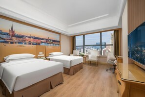 A hotel room with two beds, a desk, a chair, a TV, and a large window with a cityscape view. - Vienna International Hotel (Shenzhen Qianhai Happy Bay Hotel) (Shenzhen)