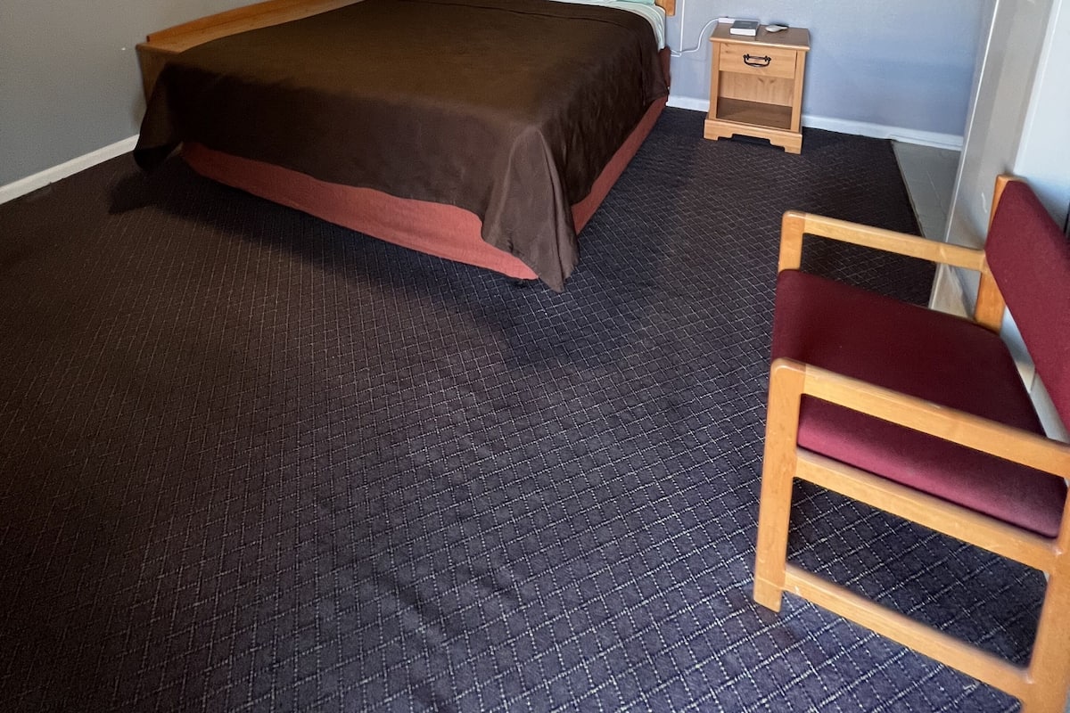 Ein Hotelzimmer mit Bett, Stuhl, Nachttisch und einem gerahmten Bild an der Wand.
