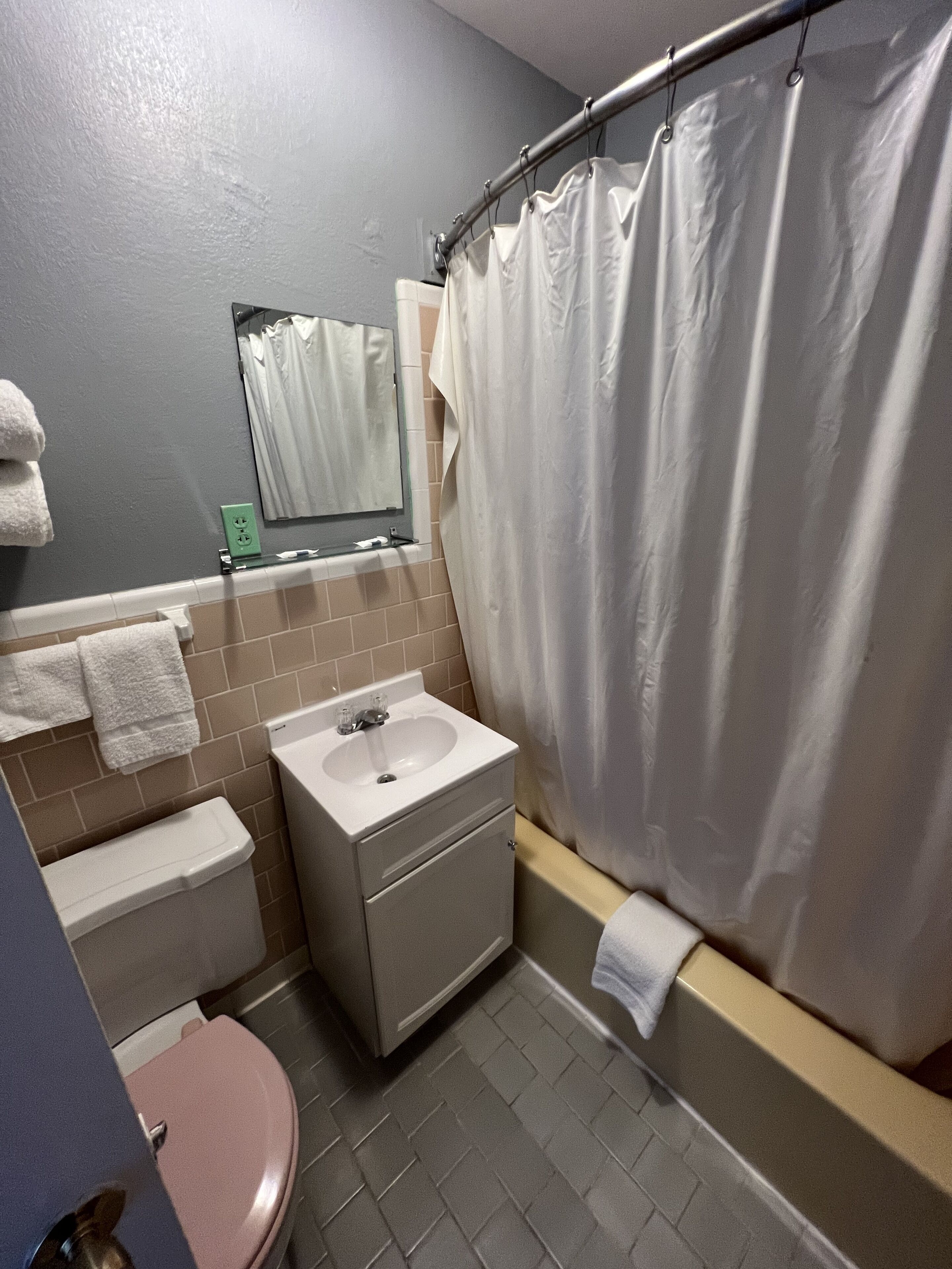 Un baño con lavamanos, espejo, inodoro y cortina de ducha.