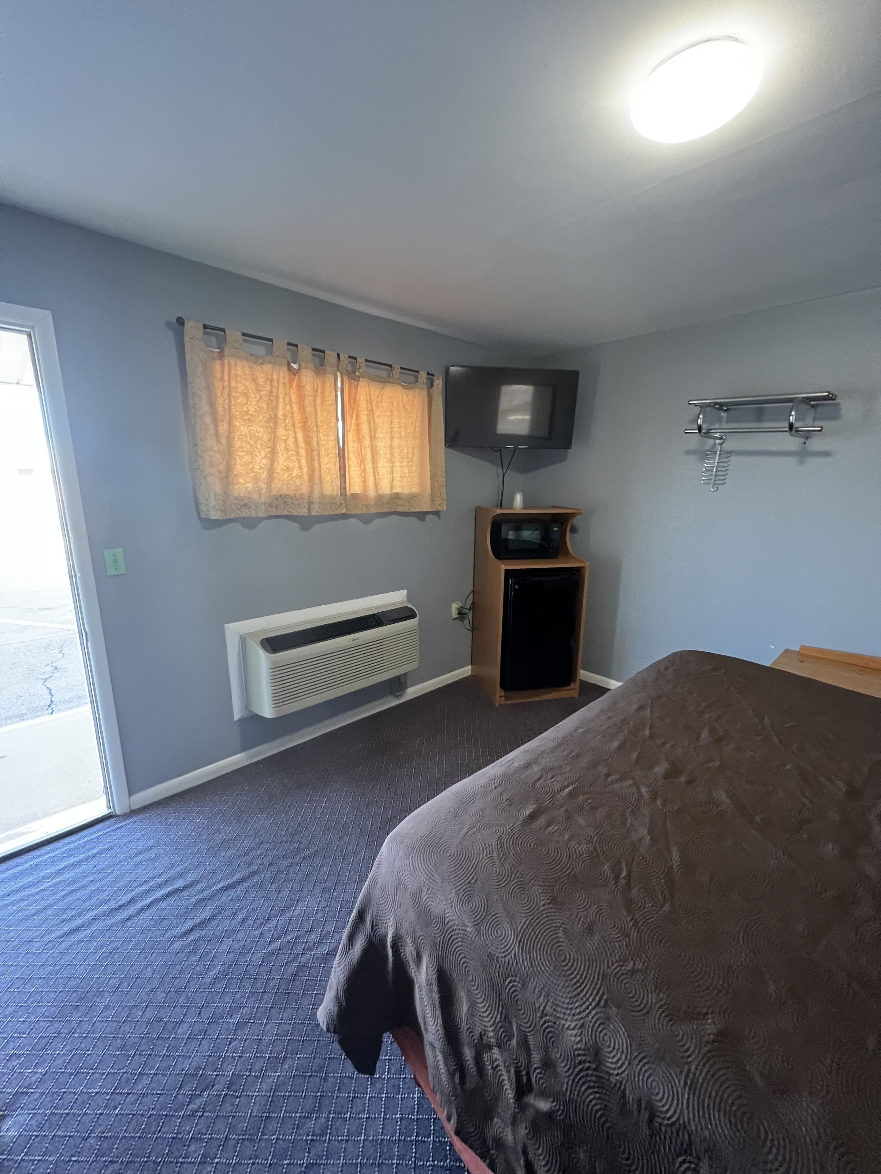 A hotel room with a bed, a TV mounted on the wall, a heater, and a window with curtains.