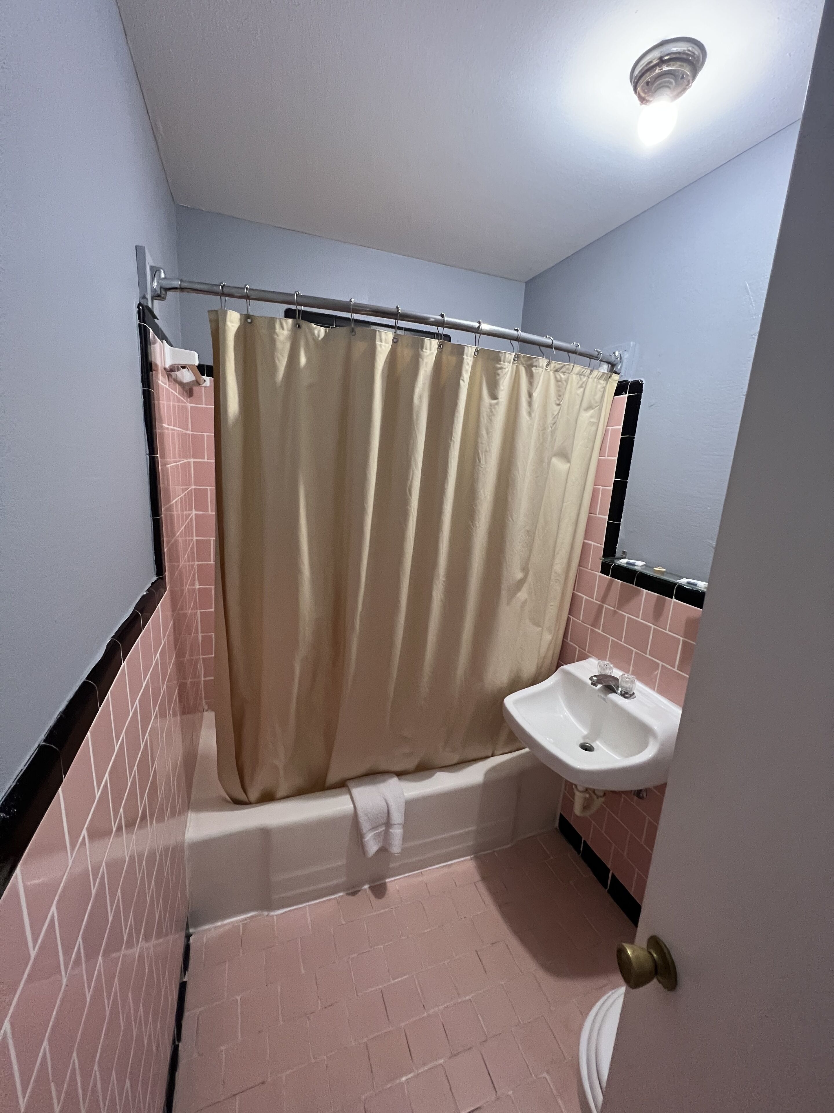 A bathroom with a shower curtain, a bathtub, a sink, and pink-tiled walls.