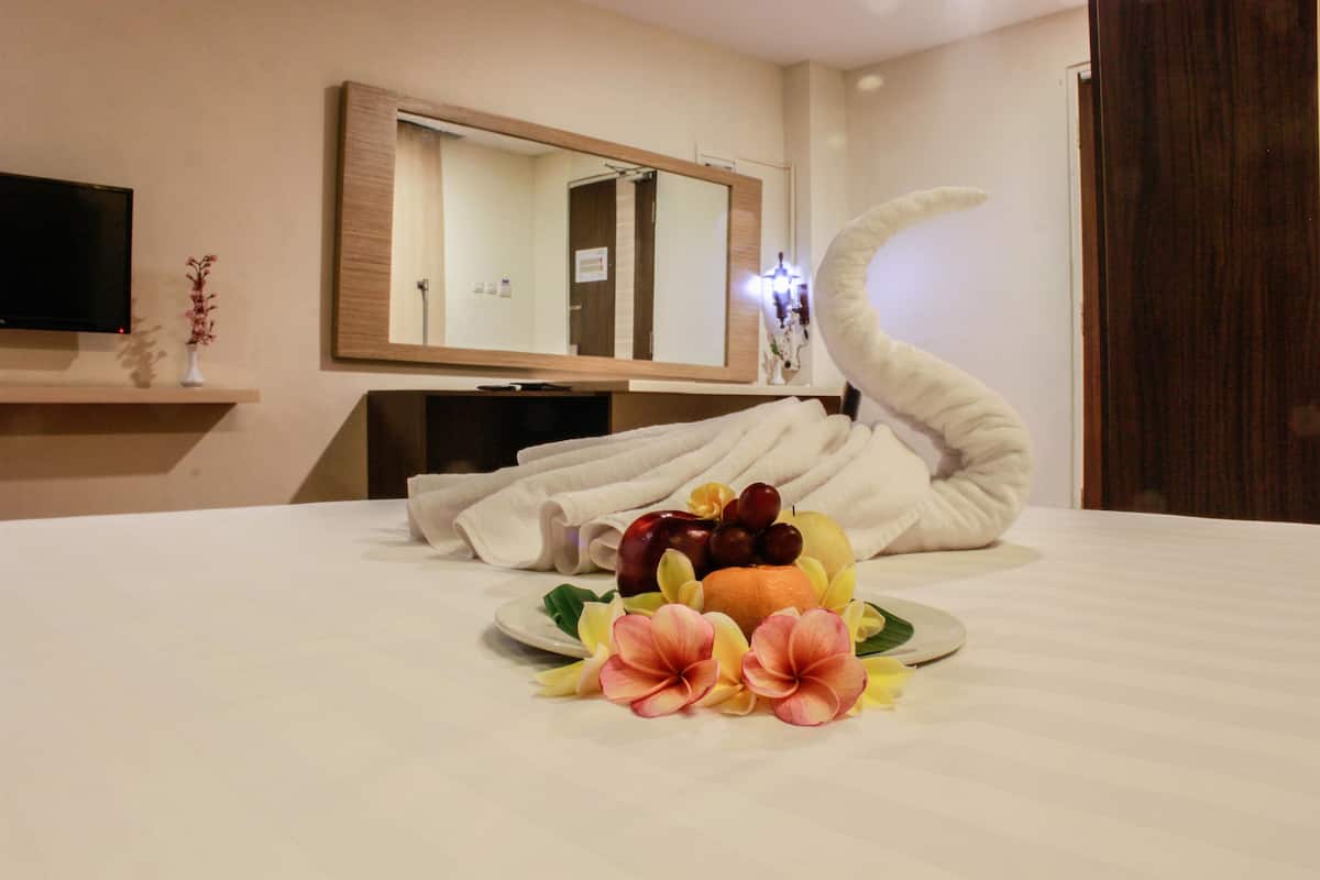 A hotel room with a neatly made bed, a fruit and flower arrangement on the bed, a television on the wall, and a large mirror.