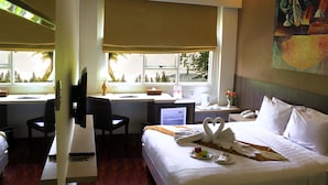 Una habitación de hotel con una cama, dos escritorios, una silla, un televisor y un cuadro en la pared.