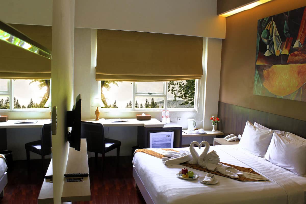 A hotel room with a bed, two desks, a chair, a TV, and a painting on the wall.