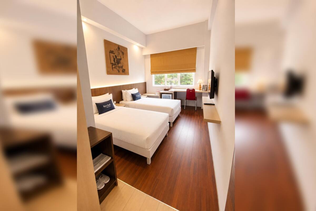 A modern hotel room with two beds, a desk, a TV, and a window.