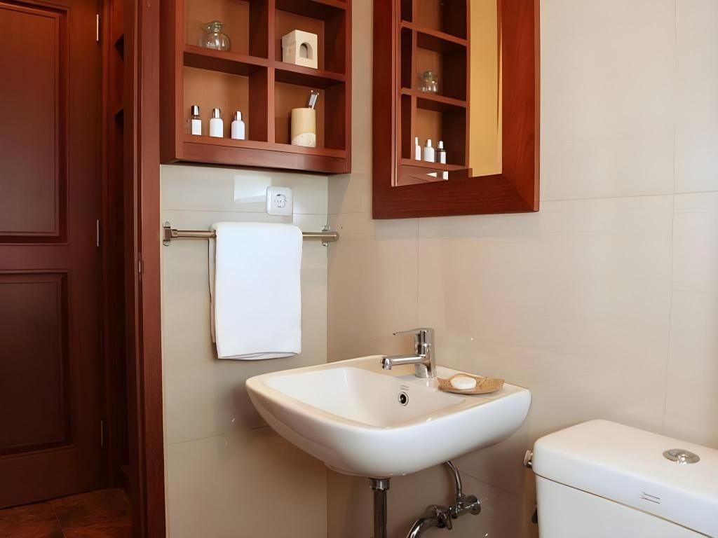 A bathroom with a white sink, a toilet, and wooden cabinets above the sink.