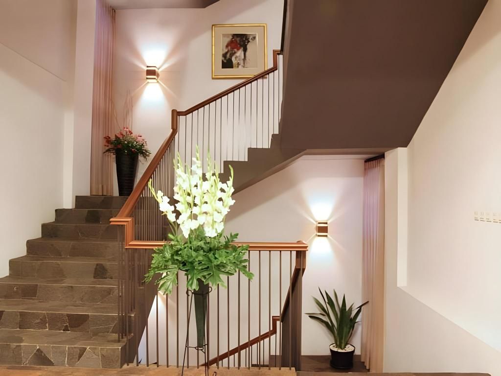A staircase with a wooden handrail, a potted plant, and a wall-mounted light fixture.