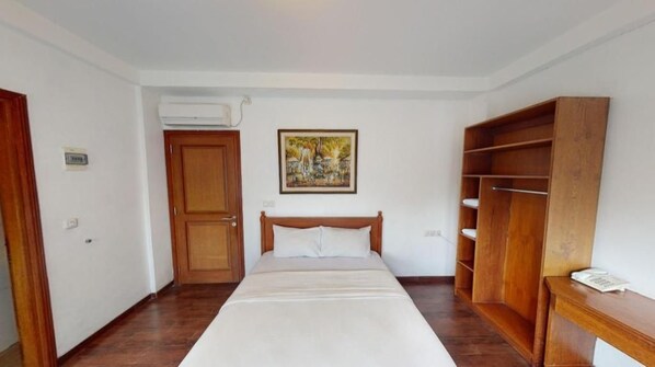 A bedroom with a bed, a wooden wardrobe, a painting on the wall, and an air conditioning unit.