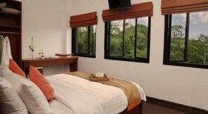 Un dormitorio con cama, escritorio y ventanas que dan a zonas verdes.