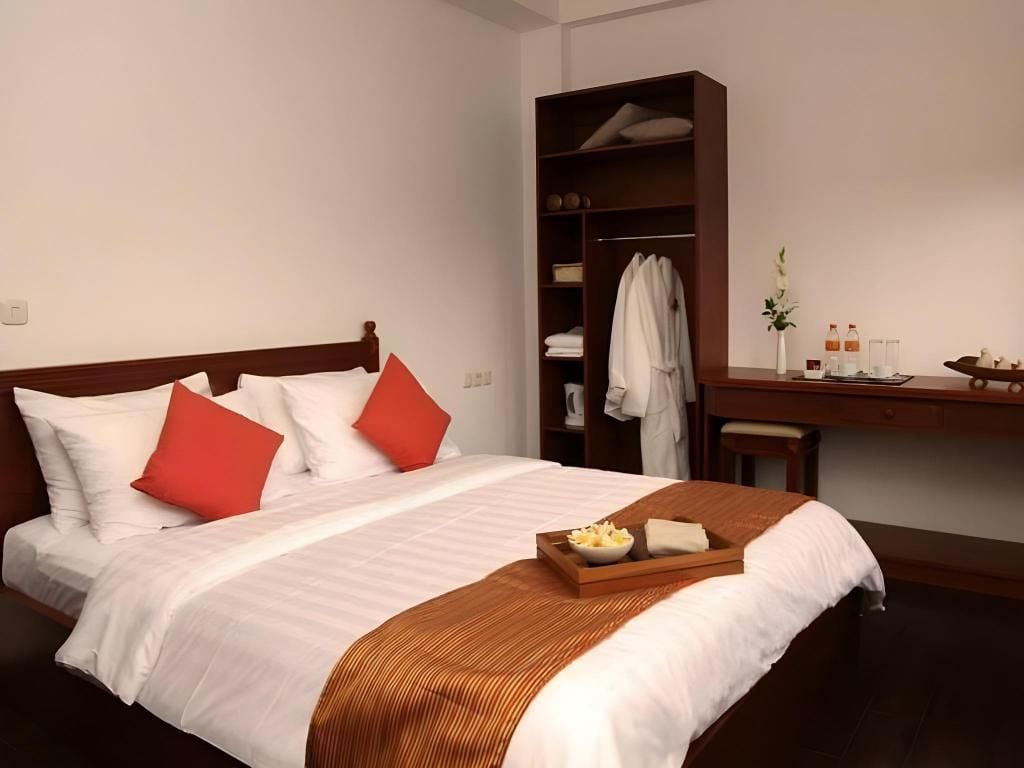 A neatly made bed with pillows, a tray with snacks, a wooden desk, and a wardrobe.