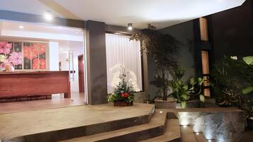 A reception area with a wooden reception desk, a staircase leading to an upper level, and a variety of potted plants.