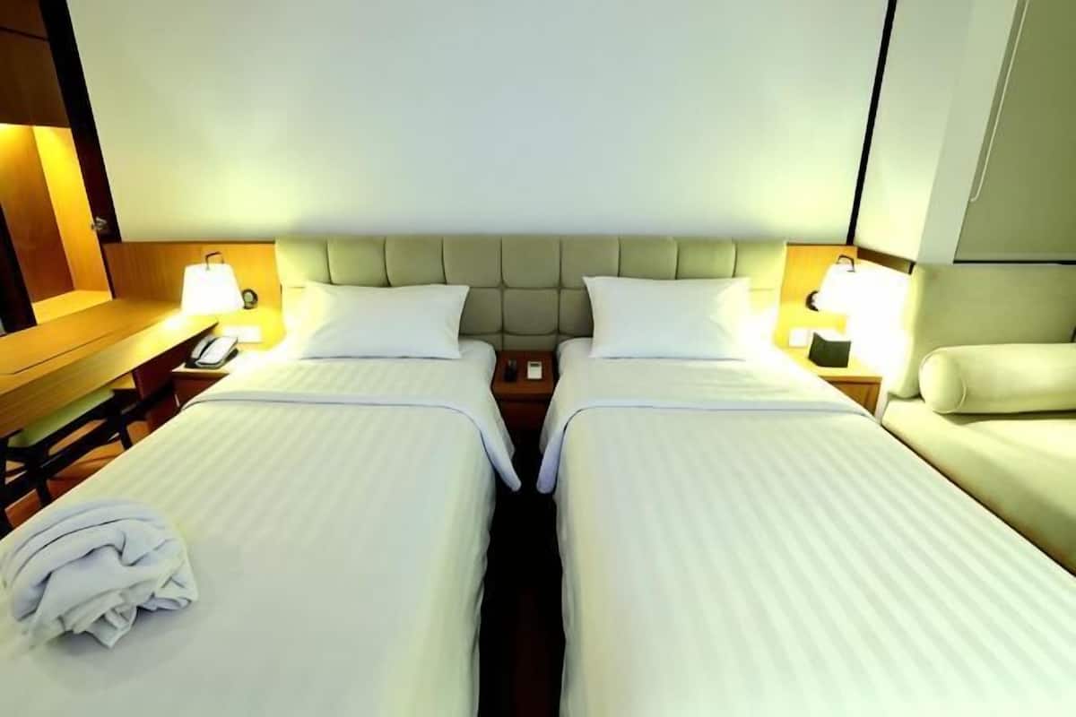 A hotel room with two beds, a nightstand with a lamp, a wooden headboard, and a sofa.