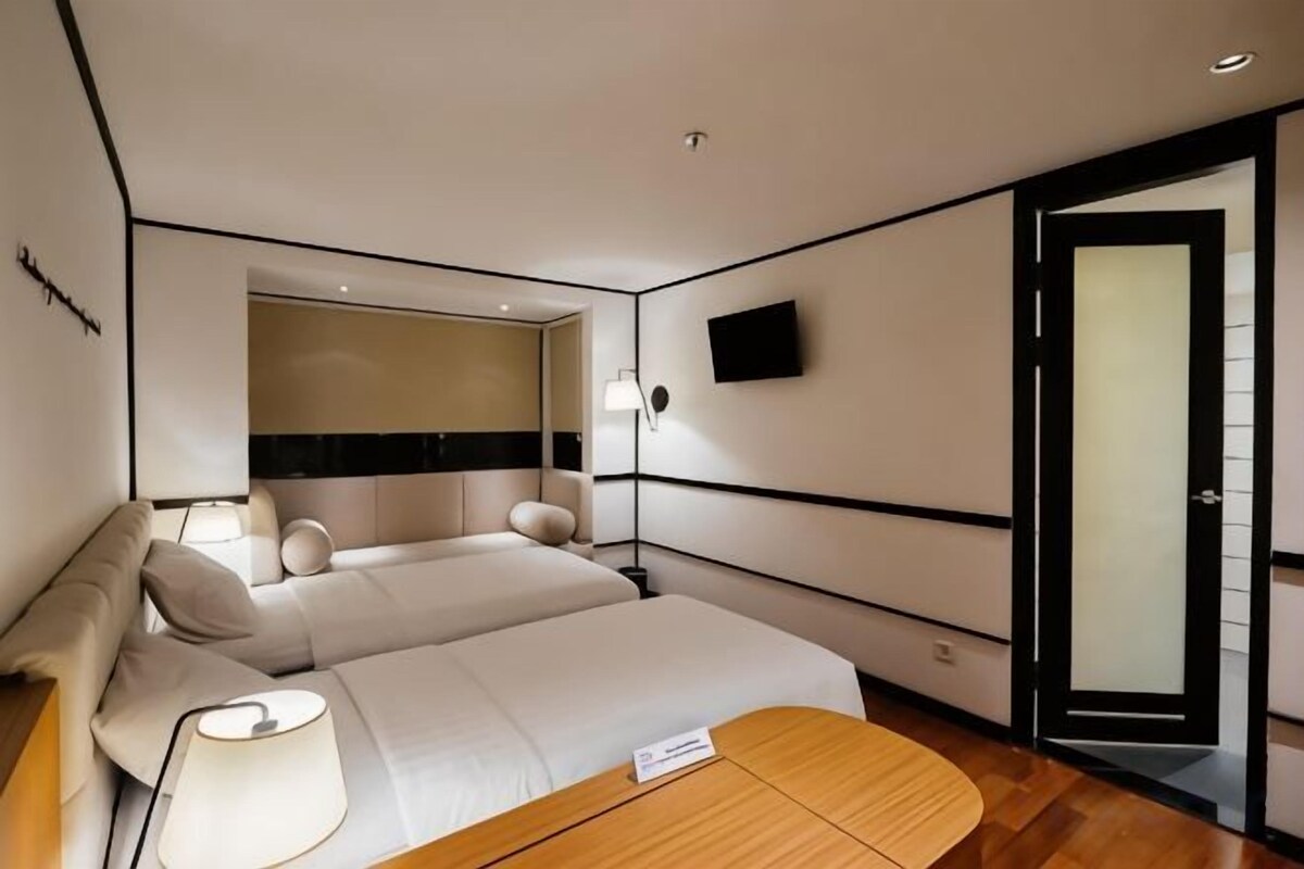A hotel room with a bed, bedside table, lamp, and a television mounted on the wall.