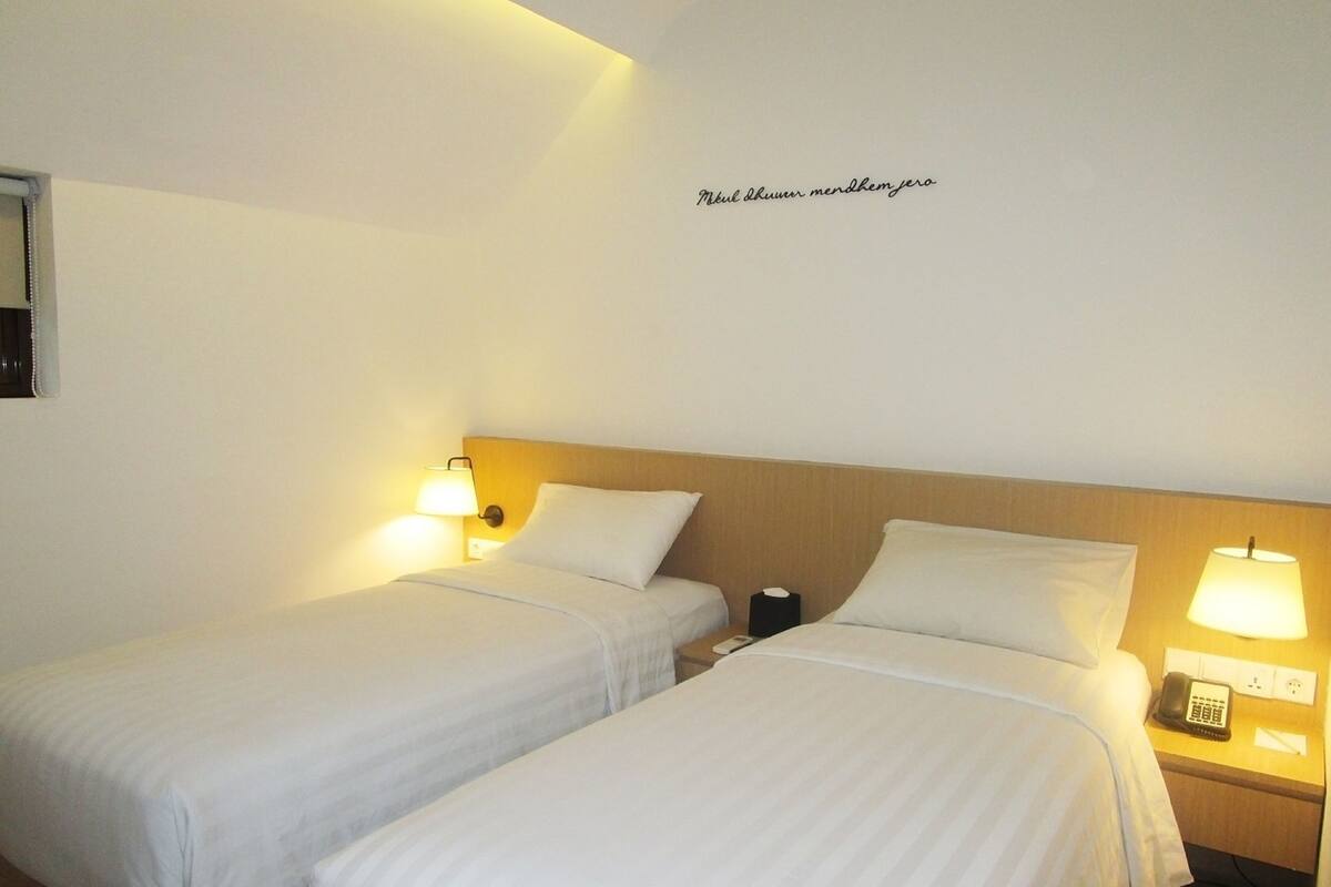 A hotel room with two single beds, bedside lamps, a nightstand with a telephone, and a wall-mounted sign.