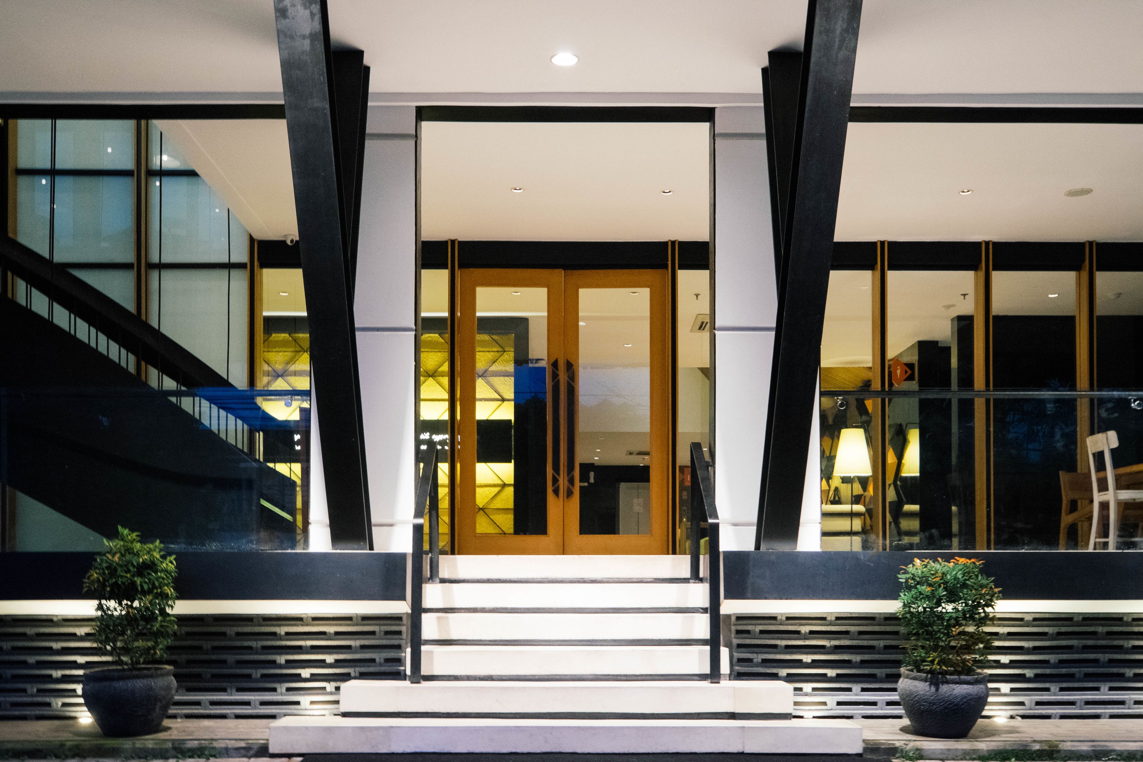 A modern building entrance with a staircase, large windows, and two potted plants.