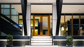 A modern building entrance with a staircase, large windows, and two potted plants.
