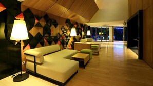 A modern hotel lobby with geometric wall patterns, a seating area with sofas and tables, and a large window offering a view of the outdoors. - Hotel Namin (Bandung)