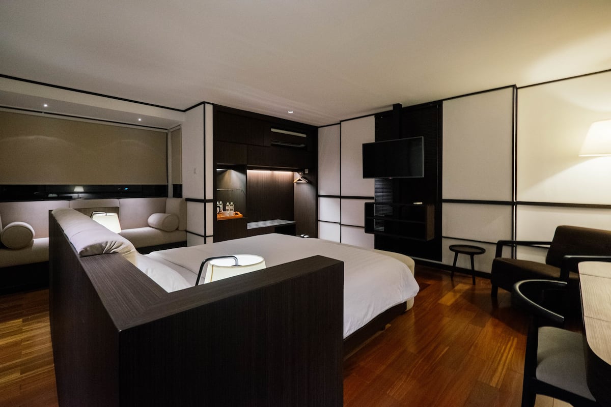 A modern hotel room with a large bed, a TV, a desk, and a seating area.