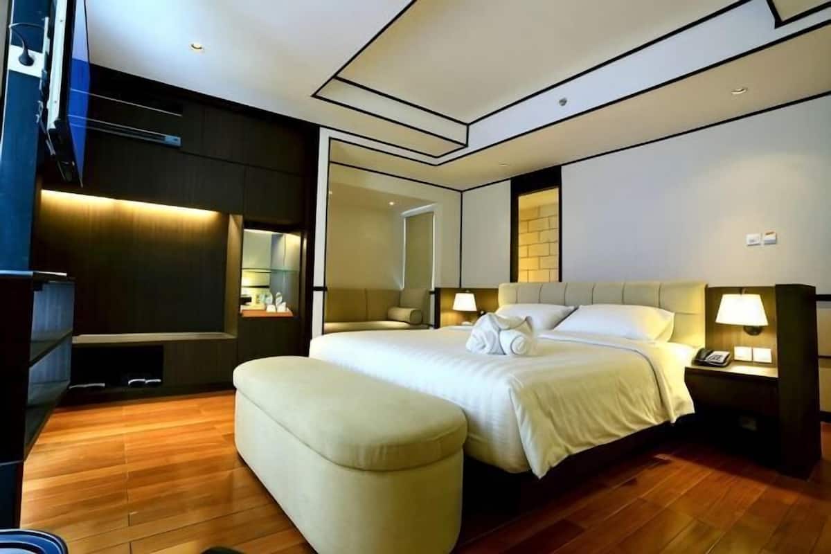A modern hotel room with a large bed, a seating area, a TV, and a mirror.