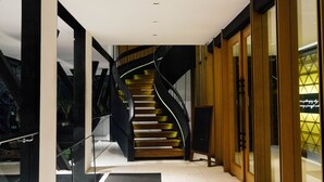 A modern interior with a spiral staircase, glass railings, and a wooden finish wall. - Hotel Namin (Bandung)