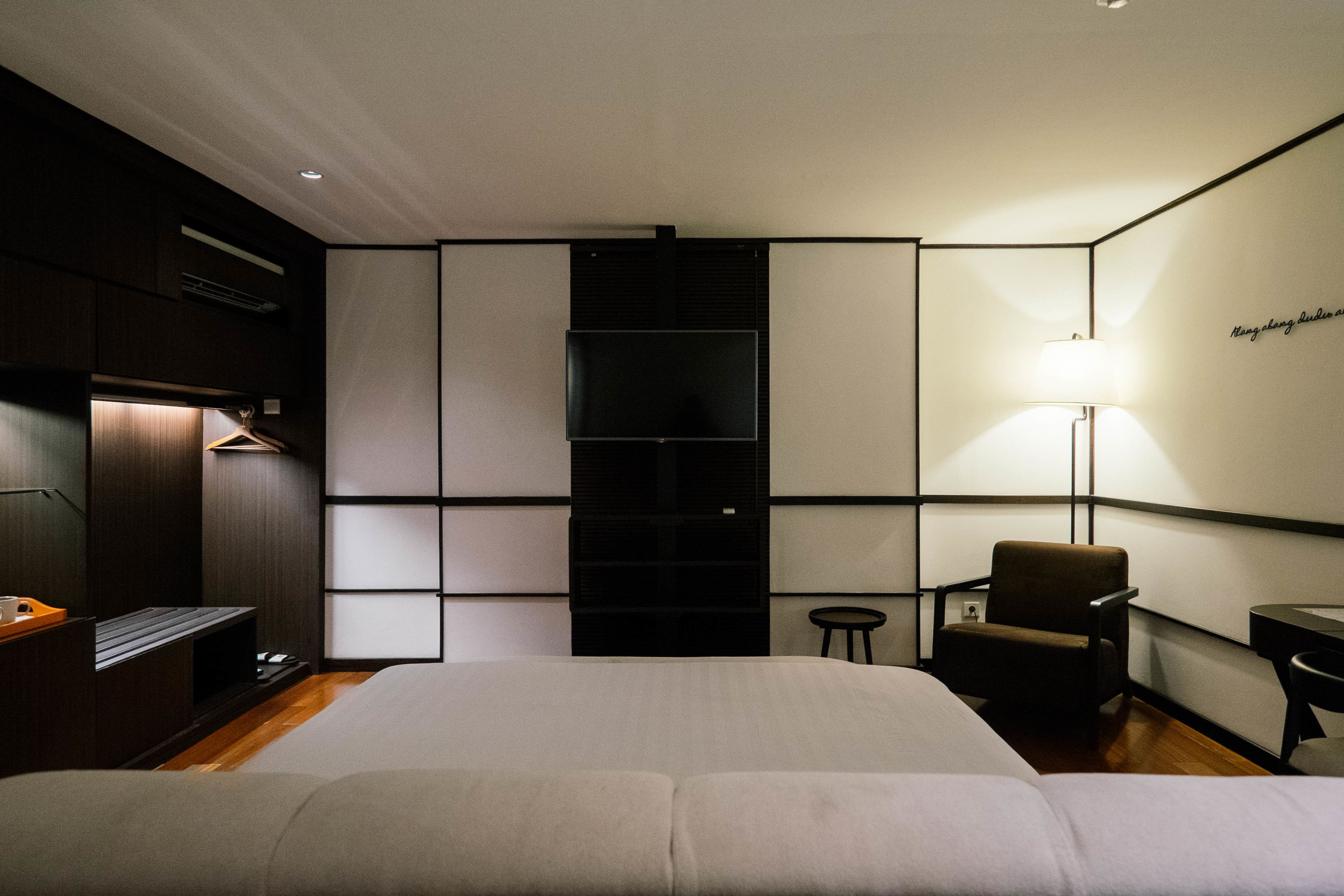 Une chambre d’hôtel moderne équipée d’un grand lit, d’un bureau, d’une chaise, d’une petite table et d’un téléviseur fixé au mur.