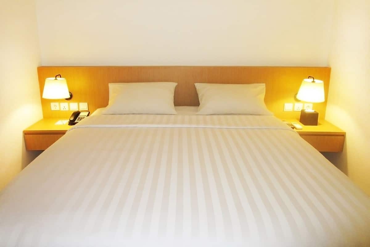 A neatly made bed with a striped bedspread, two pillows, and two bedside lamps on wooden nightstands.