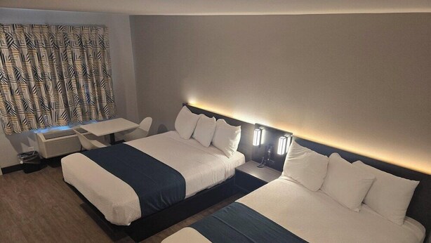 A hotel room with two beds, a desk, and a patterned curtain. - Americas Best Value Inn Downtown (Los Angeles)