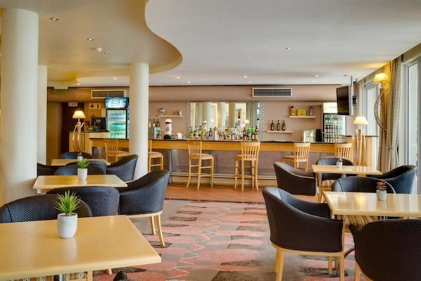 A modern hotel lobby with a bar area, seating arrangements, and a patterned carpet.