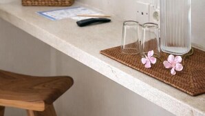 Una habitación limpia y moderna con un televisor de pantalla plana montado en la pared, un taburete de madera, un posavasos tejido, una jarrón de vidrio y dos vasos pequeños sobre la encimera.