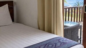 Una cama con una colcha estampada, un cabecero de madera y vistas al océano a través de una ventana con cortinas.