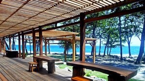 Una terraza de madera con bancos y mesas que da a una playa.