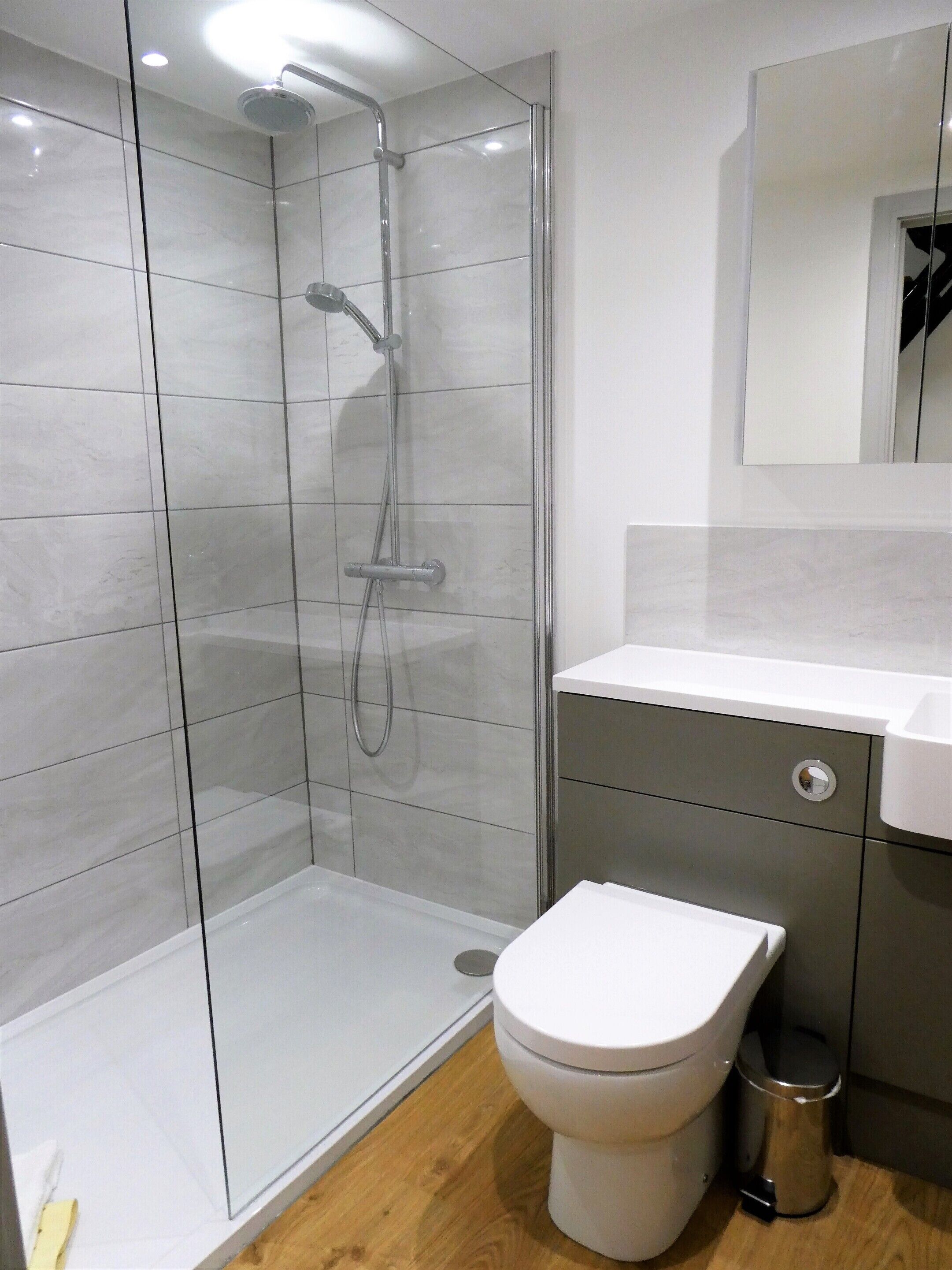 Une salle de bain moderne dotée d’une douche à parois de verre, de toilettes et d’un lavabo.