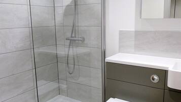 A modern bathroom with a glass-enclosed shower, a toilet, and a sink.