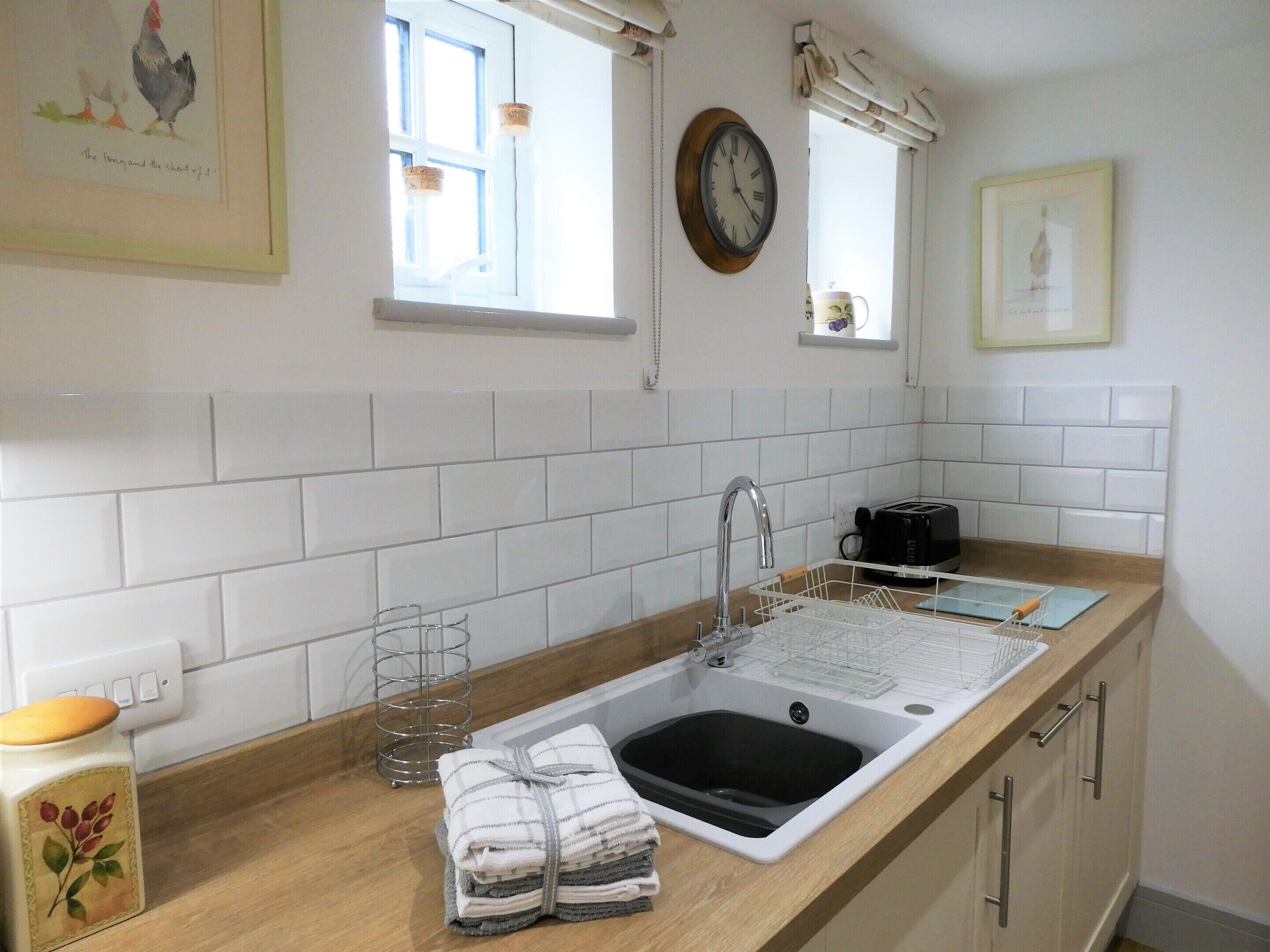 Een keuken met witte tegels, een spoelbak, een broodrooster en een klok aan de muur.