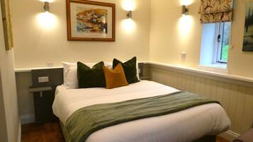 Una cama bien tendida con un edredón verde, un cuadro enmarcado encima y dos luces fijadas a la pared.