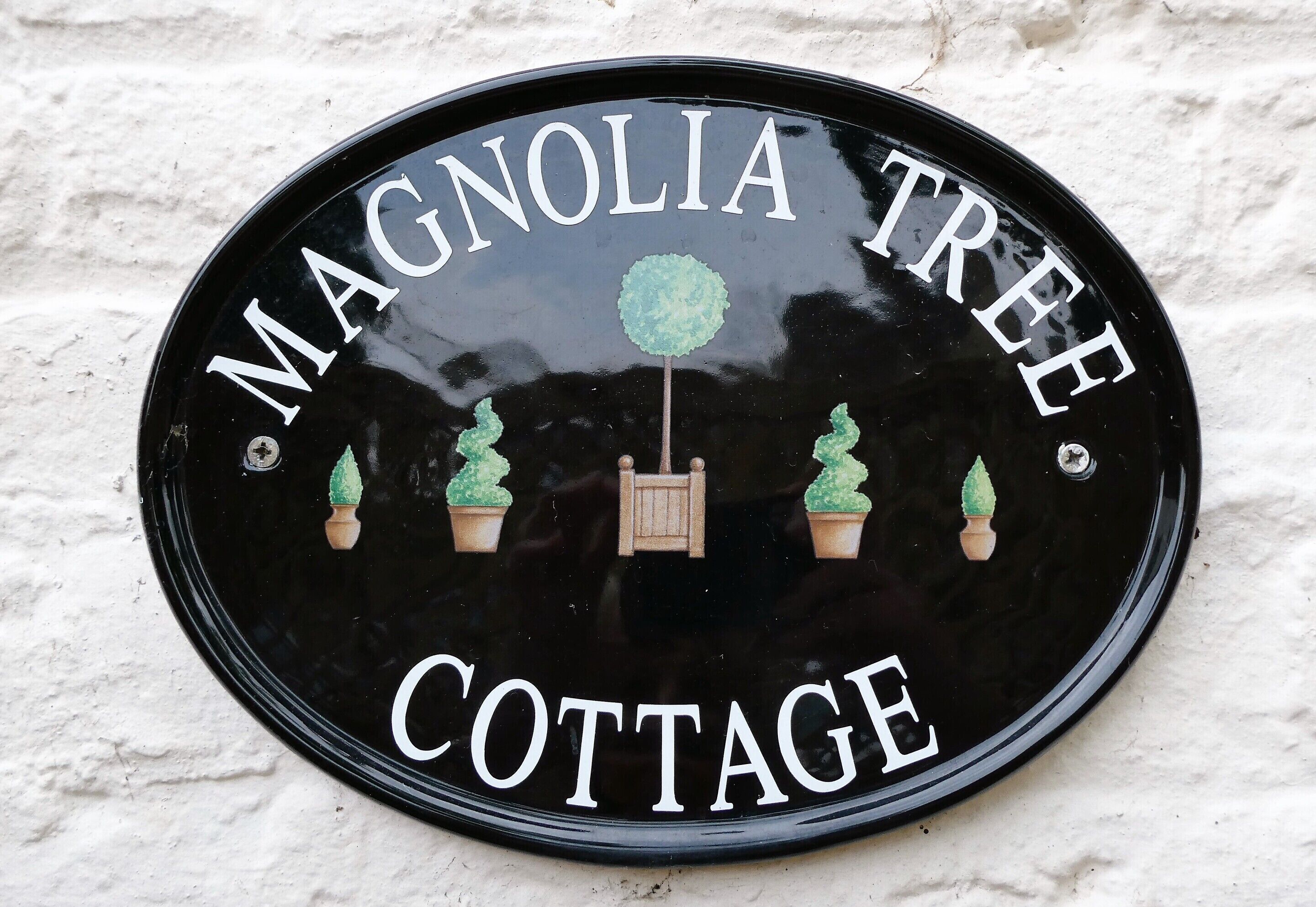 A black circular sign with white lettering stating "Magnolia Tree Cottage."
